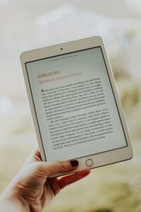 A close-up of a hand holding a tablet displaying an e-book with a visible foreword section.